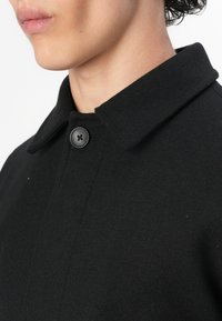 Black wool coat featuring a flat collar, single black button closure, and a structured design with smooth, clean lines.