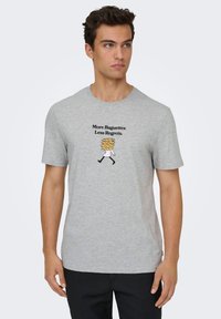 Γκρι βαμβακερό μπλουζάκι με μαύρο καρτούν σχέδιο ενός φούρναρη με μπαγκέτες, κείμενο που γράφει «Περισσότερες Μπαγκέτες Λιγότερα Μετανιώματα». Κοντά μανίκια.