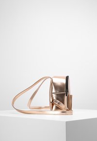 Metallinen ruusukultainen olkalaukku, jossa on vetoketjullinen osasto, litteä muotoilu ja säädettävä hihna. Sujuva pinta ja suorakulmainen muoto.