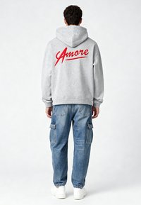 Grauer Hoodie mit "Amore" in roter Schreibschrift auf dem Rücken, kombiniert mit hellblauen Cargo-Jeans. Das Outfit wird mit weißen Sneakern abgerundet.