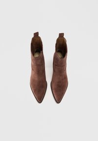 Botas de tobillo de ante marrón con punta afilada, que presentan recortes laterales y lengüetas cortas. Textura suave con un acabado mate.