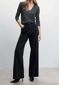 Jeans a gamba larga neri abbinati a una maglietta attillata e luccicante di colore scuro con scollatura a V. L'outfit è completato da tacchi a punta neri.