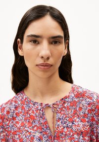 Blumenbluse in Rot, Lila und Weiß mit einem gebundenen Ausschnitt und einem leichten Stoff, der ein lebhaftes Blumenmuster aufweist.