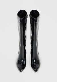 Botas de charol negras hasta la rodilla con punteras afiladas, tacones planos y cremalleras en la parte superior. Textura suave y brillante.