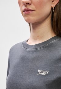 Γκρίζα μπλούζα με στρογγυλή λαιμόκοψη και κεντητό λογότυπο "tommy jeans". Λείο ύφασμα και άνετη εφαρμογή.