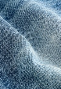 Primo piano di tessuto denim blu chiaro con texture a spina di pesce visibile e morbide pieghe che creano ombre sottili.