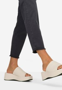 Beige plateausandalen met een open teen ontwerp, met een gladde textuur en een licht gebogen, dikke zool met groene accenten.