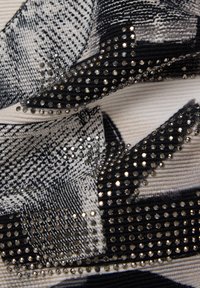 Schwarzer und weißer Stoff mit einem strukturierten Muster, verziert mit metallischen Nieten in unterschiedlichen Größen für zusätzliche Details und Dimensionen.