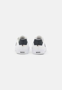 Baskets blanches avec une surface en cuir lisse, accents noirs au talon et le logo « BOSS » à l'arrière. Design simple et bas.