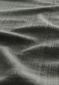 Donkergrijs, textiel met een subtiel geweven patroon, met plooien en vouwen die zachtheid en flexibiliteit aangeven.