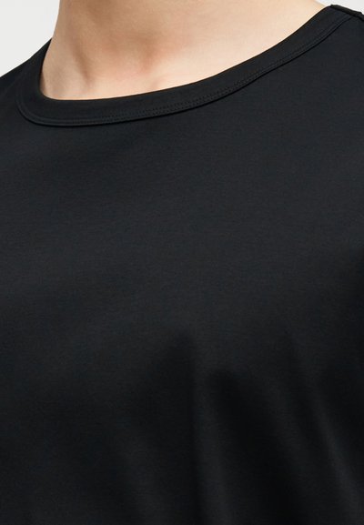 Κοντινό πλάνο ενός ατόμου που φοράει μια απλή μαύρη μπλούζα με στρογγυλή λαιμόκοψη, δείχνοντας τη λαιμόκοψη και την ανώτερη περιοχή του στήθους.