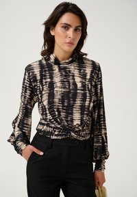 Långärmad topp med ett abstrakt mönster i svart och beige, mock-neck och knuten detalj vid midjan, kombinerad med skräddarsydda svarta byxor.