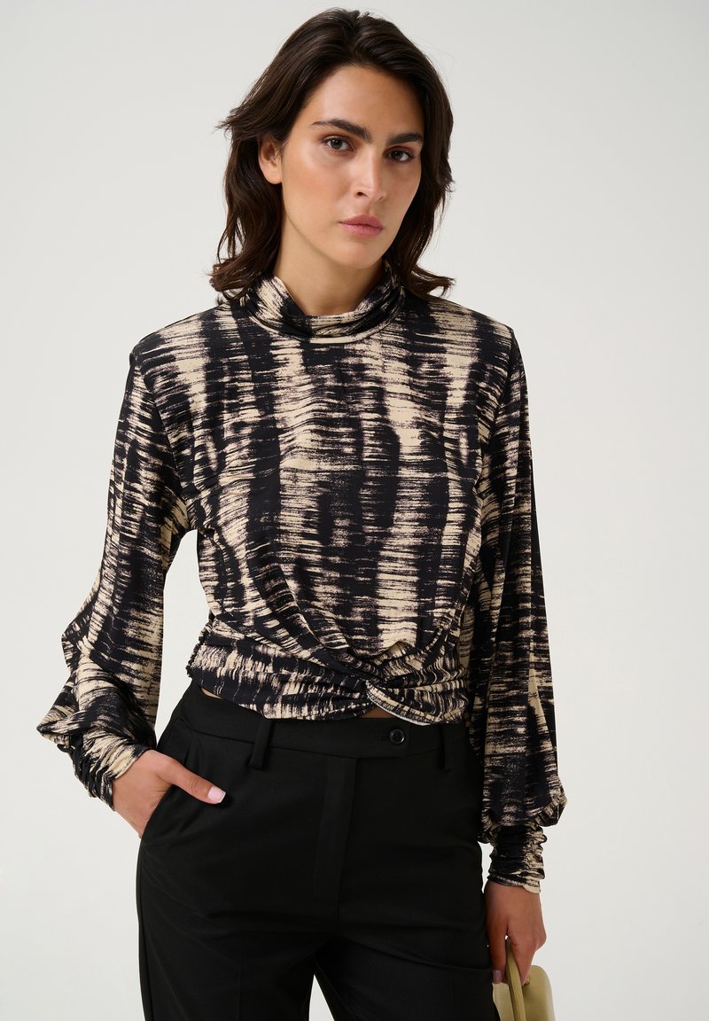 Långärmad topp med ett abstrakt mönster i svart och beige, mock-neck och knuten detalj vid midjan, kombinerad med skräddarsydda svarta byxor.