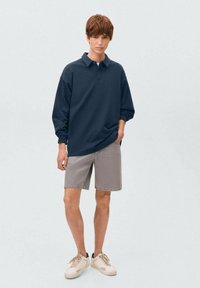 Námornícky modré polo tričko s dlhým rukávom, voľný strih, šedé denimové šortky, biele tenisky. Jednoduchý dizajn bez viditeľných vzorov alebo akcentov.