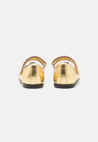 Goldene Leder-Mary-Jane-Schuhe mit einem Riemen und einer Schnalle, runder Spitze und einer schwarzen flachen Sohle, von hinten betrachtet.