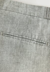 Šedá tkanina s rybí kostí. Má plochou zadní kapsu s propleteným švem. Textura působí hladce a strukturovaně.