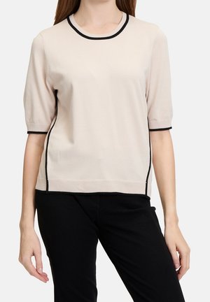 Lichtbeige gebreide top met zwarte bies bij de halslijn en zijkanten, voorzien van korte mouwen en een losse pasvorm. Soepele textuur en strak ontwerp.