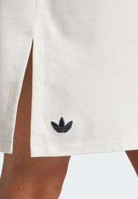 Gonna bianca in cotone con spacchi laterali e logo trefoil ricamato Adidas nero vicino all'orlo. Tessuto liscio con una vestibilità morbida.