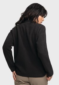 Schwarze Fleecejacke mit strukturiertem Finish, lockerer Passform und langen Ärmeln. Hat ein einfaches Design ohne sichtbare Hardware oder Akzente.