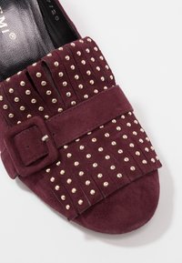 Mocassin en daim violet foncé avec dessus à franges, clous dorés et une bride à boucle en daim assortie sur le dessus.