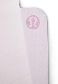 Hele roosa jooga matt nurk ümarate servadega ja roosa Lululemoni logo tekstureeritud pinnal.