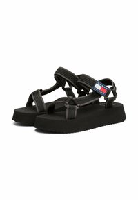 Sandalias negras fabricadas con tiras de textil y suelas de goma. Cuentan con una suela gruesa y un acento de logo en rojo, blanco y azul.