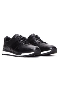 Chaussures de sport noires en cuir et maille avec une surface texturée. Présente une semelle intermédiaire blanche et un design à lacets.