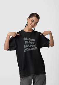 Camiseta negra de gran tamaño con texto estilizado "EL NEGRO ES MI COLOR FELIZ" en gris. Confeccionada en una tela suave y de mangas cortas.