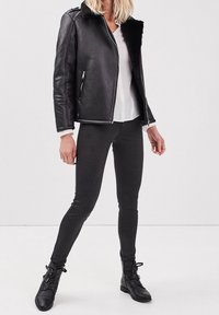 Černá kožená bunda s límcem z ovčího rouna, bílá halenka a tmavě šedé přiléhavé legíny spojené s černými vojenskými botami.