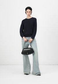 Ναυτικό πλεκτό πουλόβερ, ανοιχτό μπλε παντελόνι με φαρδιά γραμμή, κρατώντας μία μαύρη δερμάτινη τσάντα με καμπυλωτό σχήμα και ασημένιες λεπτομέρειες.