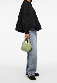 Blusa nera a balze con maniche a sbuffo, abbinata a jeans azzurri a gamba larga e una piccola borsa a rete verde. Scarpe piattaforma nere visibili.