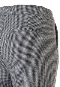 Close-up van grijs en zwart Pied-de-poule patroon op een broek, met details van de achterzak en de tailleband.