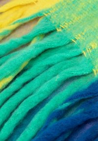 Filcowy szalik z gradientowymi kolorami żółtego, zielonego i niebieskiego. Charakteryzuje się miękkimi, teksturowanymi włóknami oraz frędzlami na krawędziach.