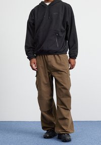 Svart fleecehuva med kenguruficka och justerbar huva, tillsammans med löst sittande khakifärgade cargobyxor med sidofickor.