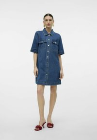 Denim skjortekjole med korte ermer, frontknaplukking, to brystlommer, blå farge og en avslappet silhuett; brukt med røde hæler.