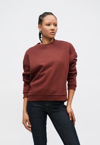 Bordeauxrød sweatshirt med rund halsudskæring, sænkede skuldersømme og ribstrikkede manchetter. Fremstillet af glat stof, kombineret med mørke denimjeans.