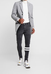 Gray tailored blazer, white turtleneck, black jeans with textured stripes and white accents, paired with white and gray sneakers.