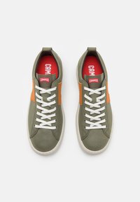 Gröna sneakers med orange detaljer, vita snören och röda innersulor. Tillverkade av ett slätt material med rund tå och texturerad dekoration.
