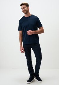 T-shirt blu navy a maniche corte abbinato a pantaloni scuri e scarpe da ginnastica nere alte. Il tessuto sembra liscio con un design a vestibilità rilassata.