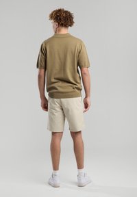 Khaki lyhyet hihapaito, jossa ribbed kaulus, yhdistettynä kerma-valkoisiin shortsseihin ja valkoisiin lenkkarit. Suora pinta, rento istuvuus ja yksinkertainen muotoilu.