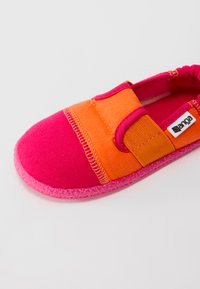 Bērnu slīdējamās kurpes spilgti rozā un oranžā audumā ar strukturētu rozā zoli un elastīgu siksniņu pāri augšai.