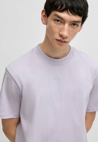 Tricou din bumbac de culoare violet deschis, cu mâneci scurte și guler rotund, având un logo discret HUGO brodat pe față, în aceeași nuanță.