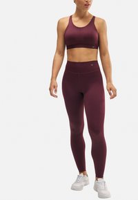 Sujetador deportivo burdeos y leggins de tiro alto a juego, ambos hechos de material elástico, combinados con zapatillas deportivas blancas.