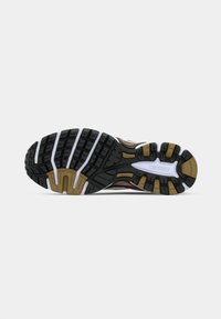 Semelle de chaussure de sport en caoutchouc noir avec un motif texturé, présentant des accents blancs et dorés, et une conception durable et flexible.
