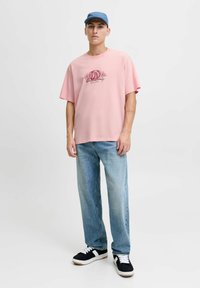 Lyserød bomulds T-shirt med grafisk print, parret med lyseblå lige ben jeans og sorte sneakers med hvide detaljer. Casual kasket bæres.