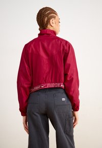 Red, cropped jacket with a high collar, elastic waistband featuring "Nike Sportswear" logo, paired with dark gray cargo pants.