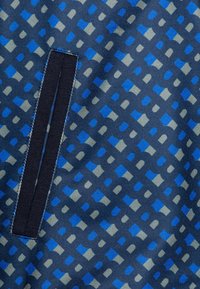 Textilie má tmavě modrou podložku s geometrickými vzory v světle modré a šedé barvě. Obsahuje vodorovný námořnický zip. Měkká textura.