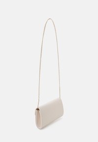 Liten beige vävd clutch med en lång, tunn guldkedja, upphängd mot en vit bakgrund.