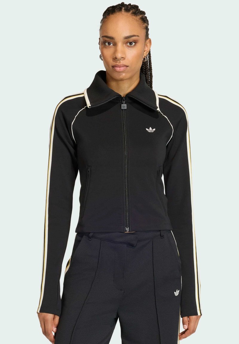 Sort lynlåstrøje med høj krave, der har kontrasterende hvide og gyldne striber på siderne samt et broderet logo på brystet.