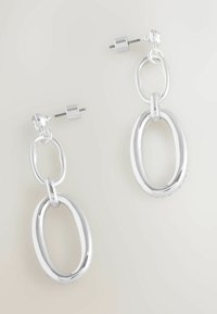 Stříbrné visací náušnice se dvěma propojenými oválnými smyčkami a zapínáním na náušnice na pozadí v neutrálních barvách.